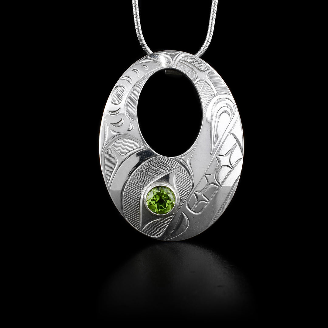 This peridot pendant is made from sterling silver, is oval shaped, and has an oval cutout in the center. There is a depiction of the Bear carved into the pendant and a peridot gemstone embedded in the Bear's eye.