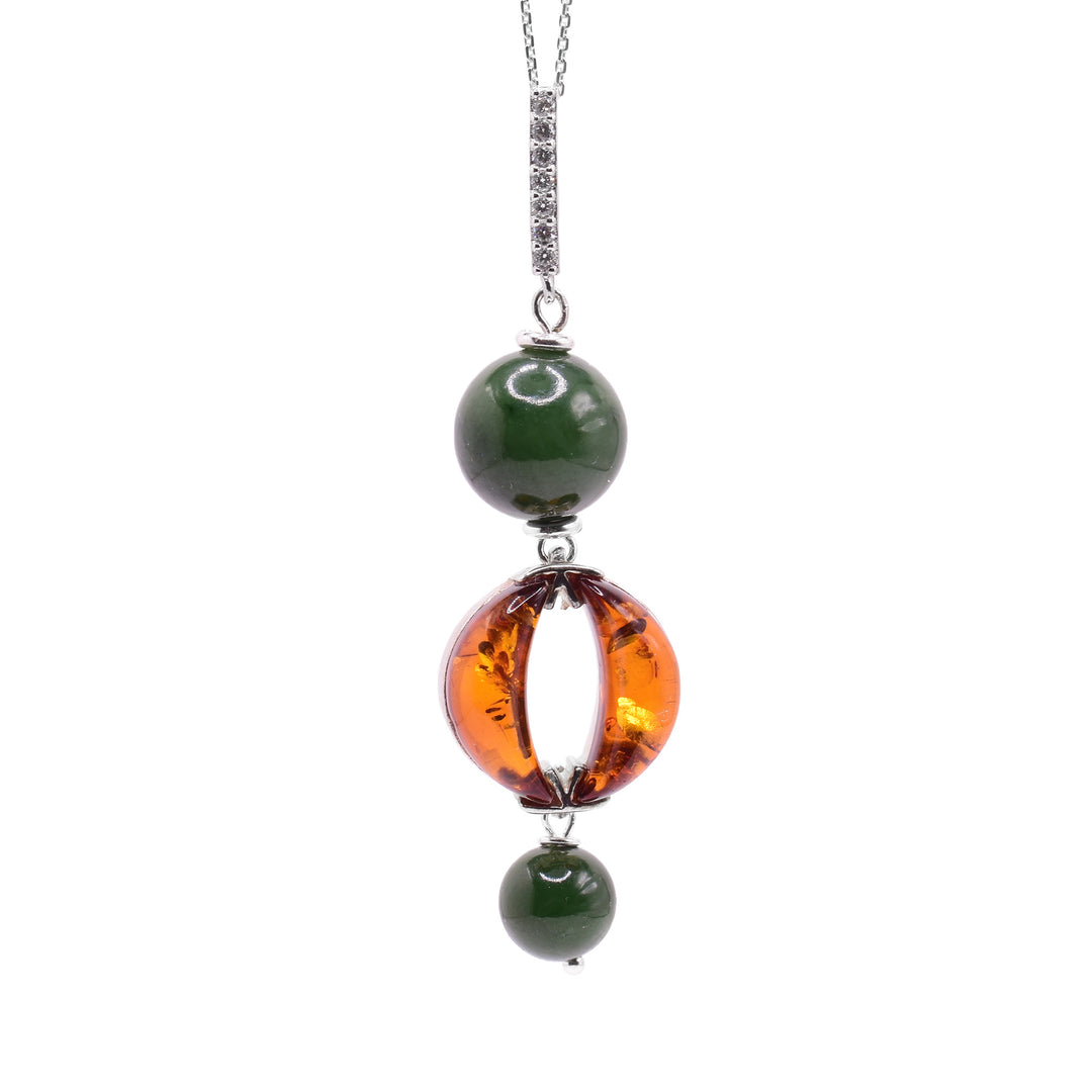 This amber pendant has a long, thin bail with cubic zirconia studded into it. Below the bail is a large, sphere shaped jade bead and an amber eye below that. There are two oval pieces of amber that make up the eye and a much small sphere, jade bead below it. The pieces are dangling from sterling silver pieces.