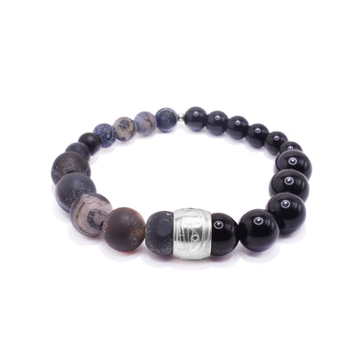This gemstone bracelet is made up of dark colored jasper and agate beads. The beads taper in size in the back and there is a sterling silver spirit bead in the front of it. There is a depiction of the Orca carved into the spirit bead.