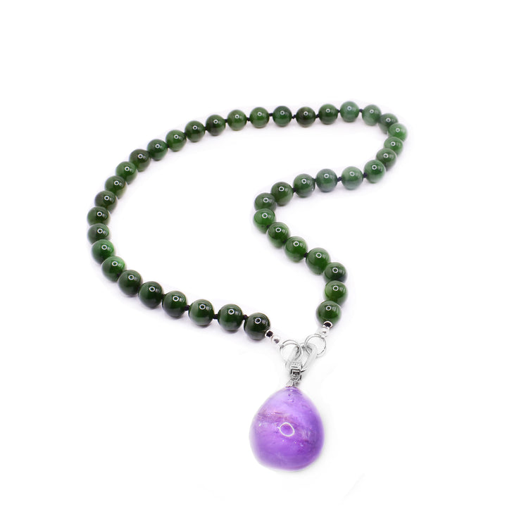 This jade beaded necklace has sphere shaped jade beads that are separated with spacers. There is a sterling silver chain link with a detachable amethyst pendant that is teardrop shaped.
