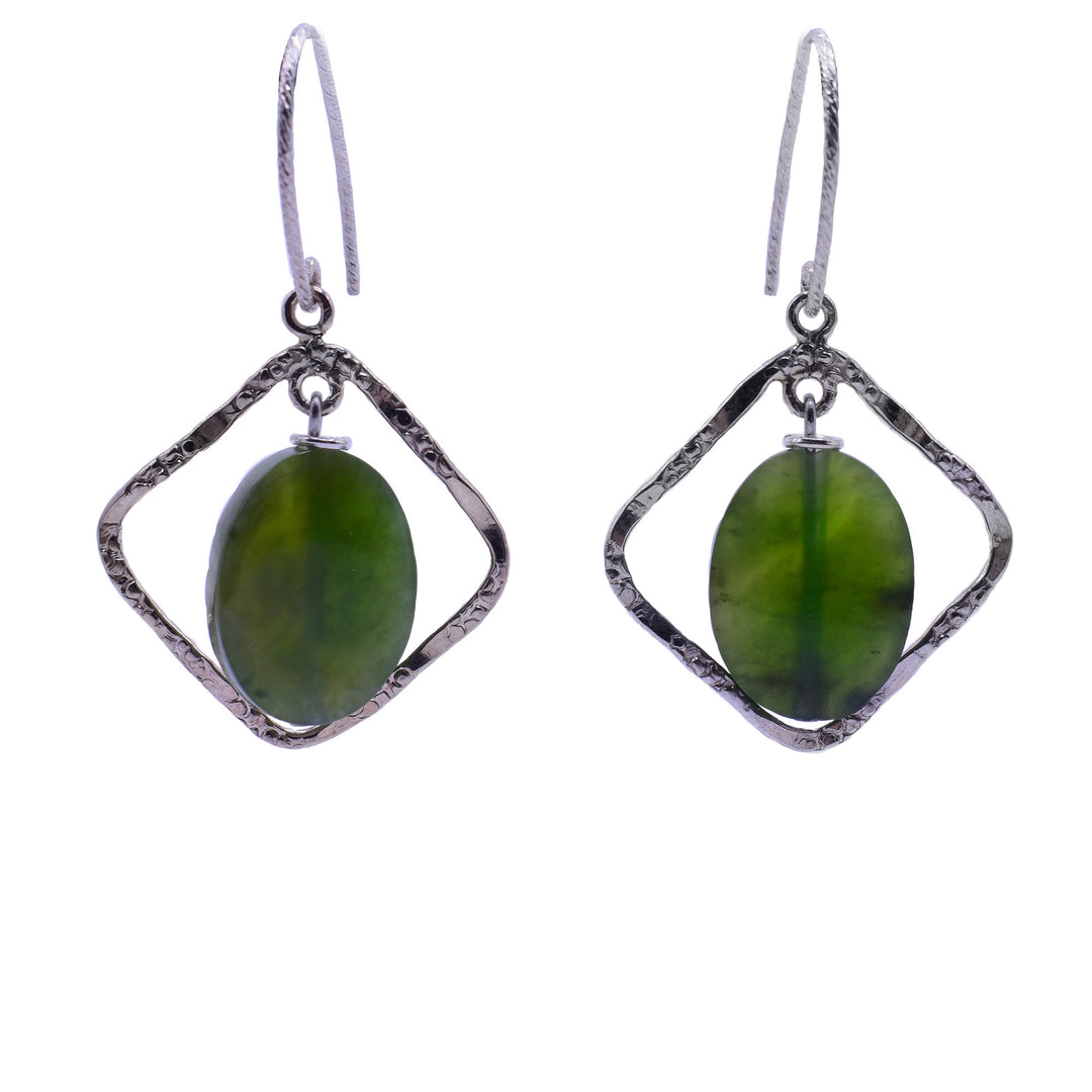 The oval BC Jade suspended within a textured, twisted, diamond-shaped silver frame. The stone is a transparent dark and light green. The silver frame has a hammered or textured surface.
The diamond dangling jade earrings are attached to a simple, looped silver ear wire.