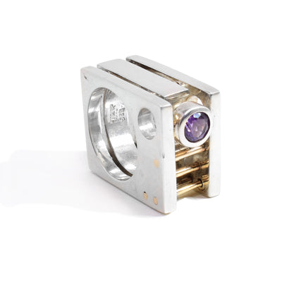 This abstract, square silver ring has three sterling silver layers with an amethyst gemstone between them. By the gemstone, there are three 14K gold rods running through two bands. The entire ring is square shaped.