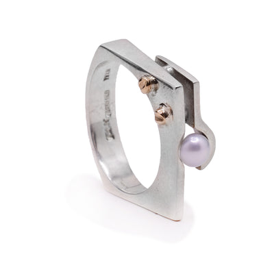 This sterling silver ring is square shaped and has a fresh water pearl held in the top by another square piece. At the top of the ring are two 14K rose gold studs.