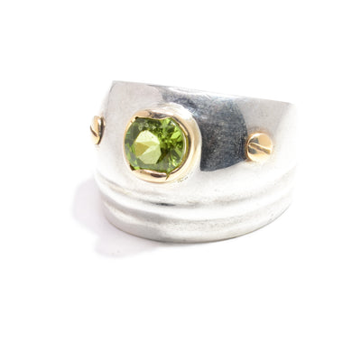 This sterling silver and gold ring has a wide, tapered band. On it is a peridot gemstone surrounded by 14K gold with gold studs on both side of the gem.