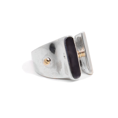 This sterling silver signet ring has a tapered band and a gap at the top of the ring. On the signet is a polished plexiglass embellishment and 14K rose gold studs.