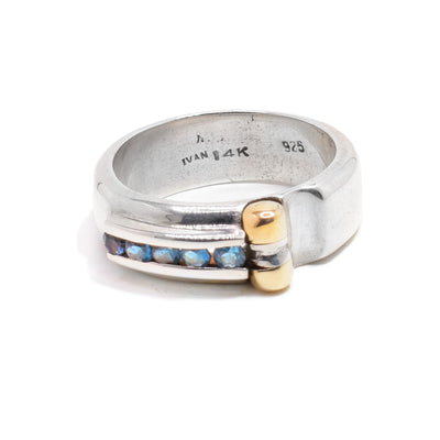 An abstract shaped silver band with five small round blue topaz stones and a 14K gold detail.