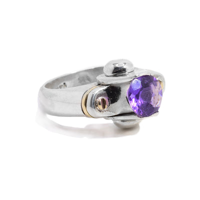 This chunky amethyst ring is made from sterling silver and has two 14K gold studs and a gold band on the signet of the ring. There are two silver half spheres holding a large amethyst gem.