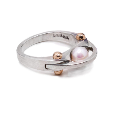 A sterling silver band with a pearl in the middle and four gold  bolt details. There is a thin silver band going over the pearl.