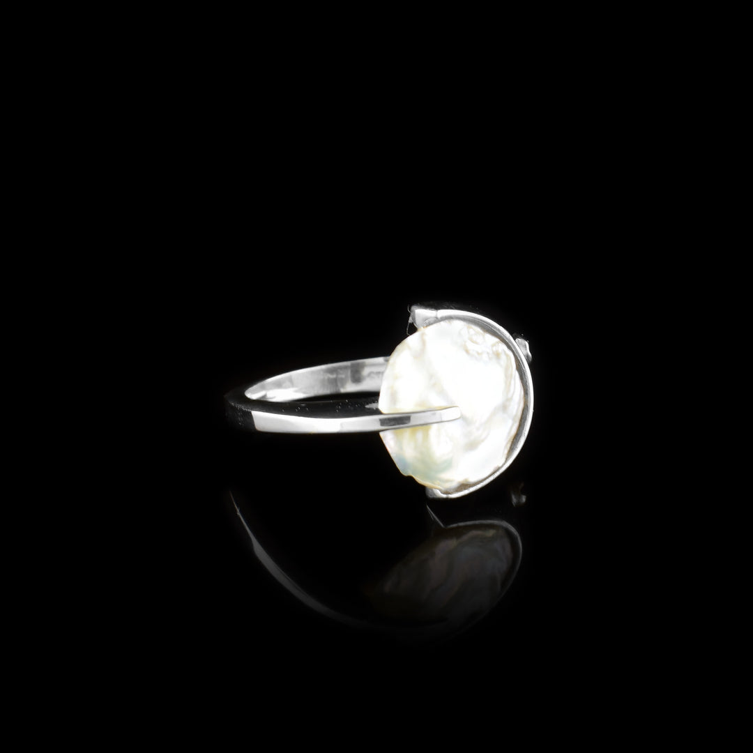 This pearl signet ring has a thin, sterling silver band and a large, flat pearl that acts as the signet for the piece. The silver band widens at the top and wraps around the circumference of the pearl. There is a 14K gold stud on the wide part of the band.
