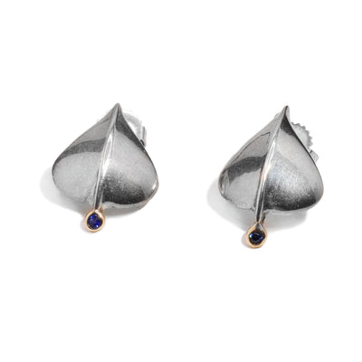 These sapphire stud earrings are made from sterling silver and are oval shaped with a sapphire gem wrapped in 14K gold.