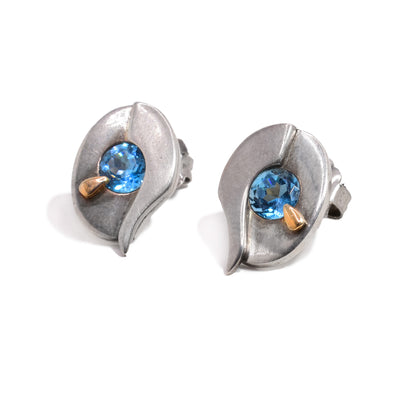 These sterling silver topaz stud earrings are teardrop shaped and have a topaz gem embedded in the middle of each earring. Beside each gem is a decorative 14K gold stud.