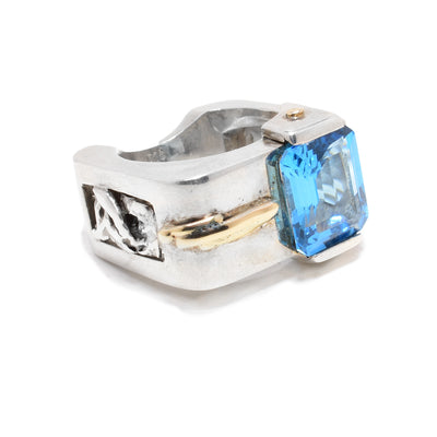 This sterling silver ring is square in shape and has a big square blue topaz stone in the front. There is a 14K gold detail to the side of the stone.