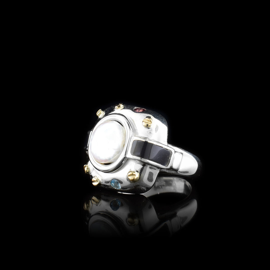 This chunky pearl signet ring has a wide, sterling silver band and at the top of the ring there is a large, rounded square made from silver. There is a large, freshwater pearl in the center of that square. There are 14K gold studs around the pearl with a blue topaz and garnet gem there too. Extending from the pear, there are rectangle, plexi glass pieces that contrast the pearl.