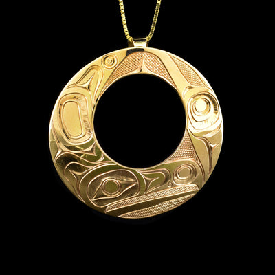 This 14K gold pendant is circle shaped and has a circle cutout in the middle of it. There is a depiction of the Raven carved into the surface of the pendant. 