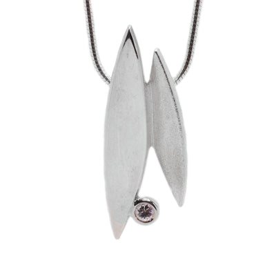 This sterling silver necklace has a round chain. The pendant consists of two sharp oval shapes attached together with a cubic zirconia gemstone attached at the bottom.