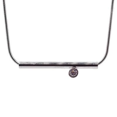 This sterling silver necklace has a round chain and a long, thin cylinder pendant. Attached to the pendant is a cubic zirconia gemstone encased in silver.