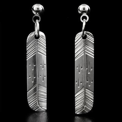 These sterling silver stud dangle earrings have feathers on them. The middle part of the feather is smooth and has two carved details on each side of the feather. The top and bottom sections have diagonal lines engraved on them.