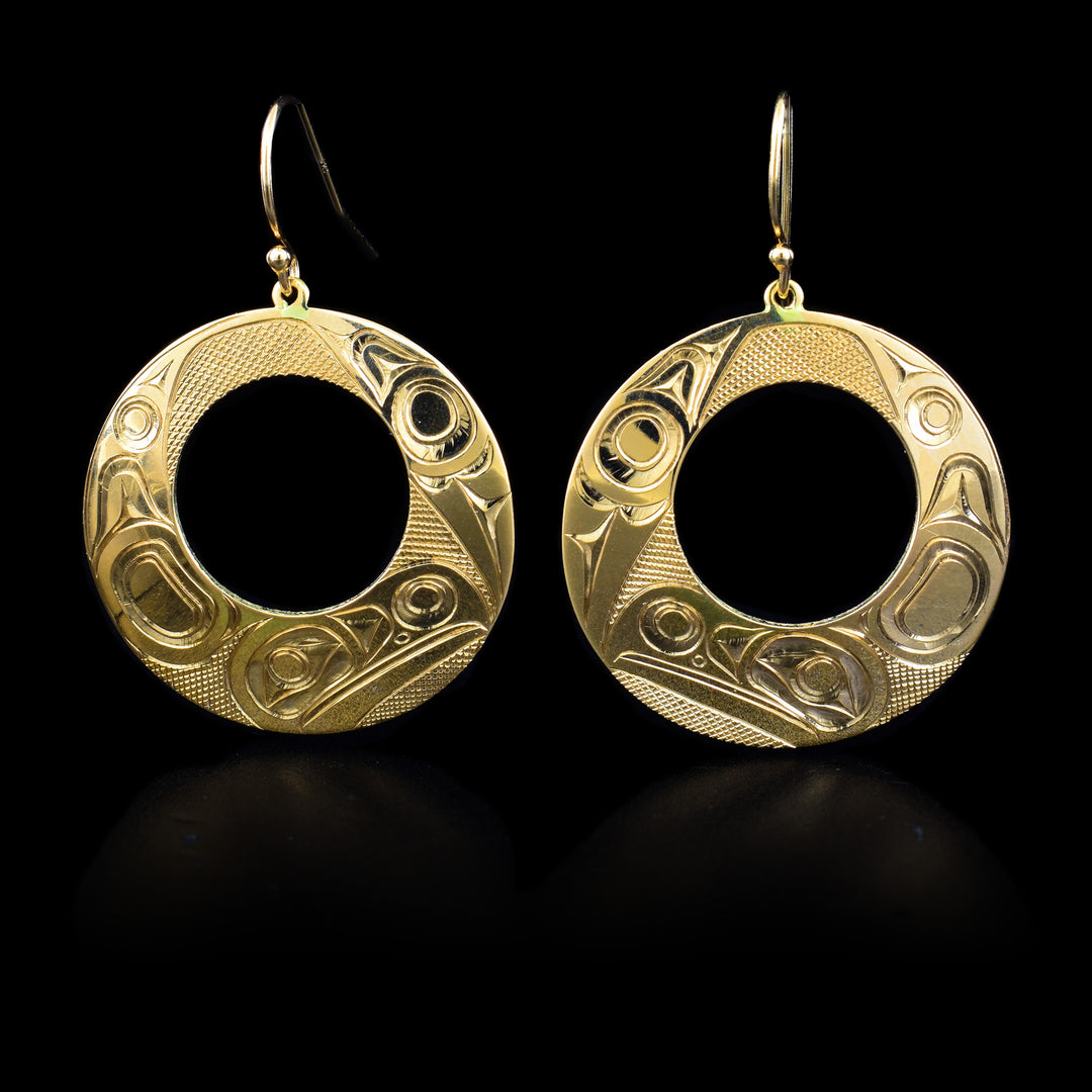 These 14K gold Raven earrings have large, circle hangs with cutouts in the middle of them. There are depictions of the Raven carved into the surface of them.