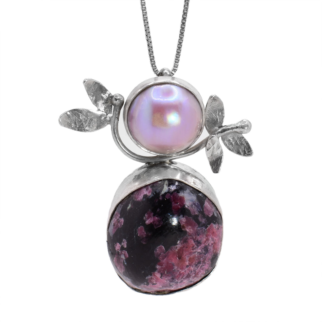 This Eudialyte and mother of pearl necklace has two, round stones stacked on top of each other. The gems are held in sterling silver and there are decorative branches made from the silver.