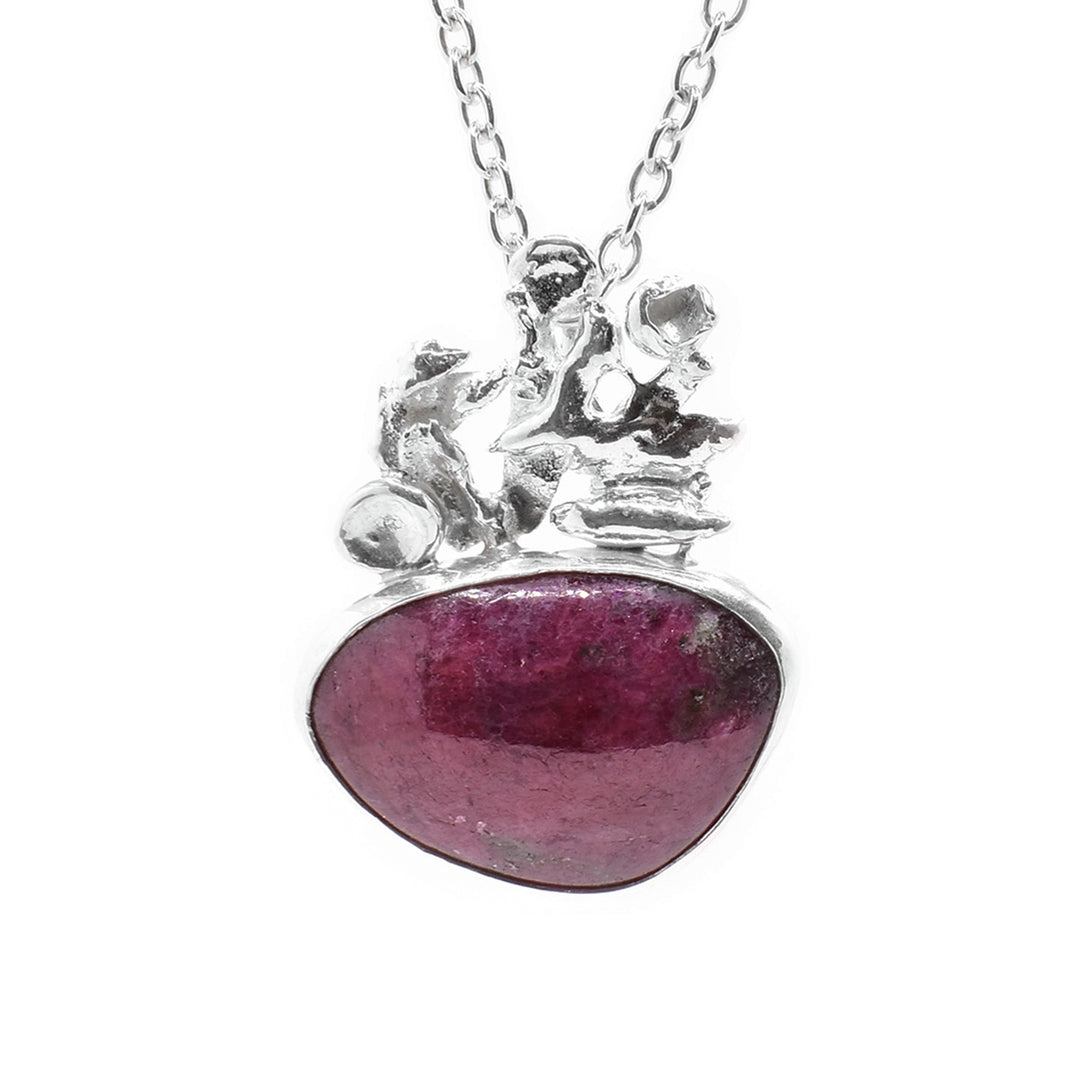 This ruby zoisite necklace has a sterling silver piece above the gem. This piece is abstract shaped, and below it is an oval shaped ruby zoisite gemstone.