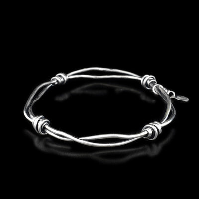 This wire bangle bracelet is made from sterling silver and has two, twisted wires with silver wrappings in the four ends of the piece.