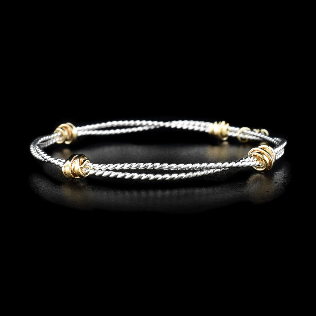This silver bracelet bangle is made out of two sterling silver coils that are attached together with four areas of gold fill wrapped around the coils.