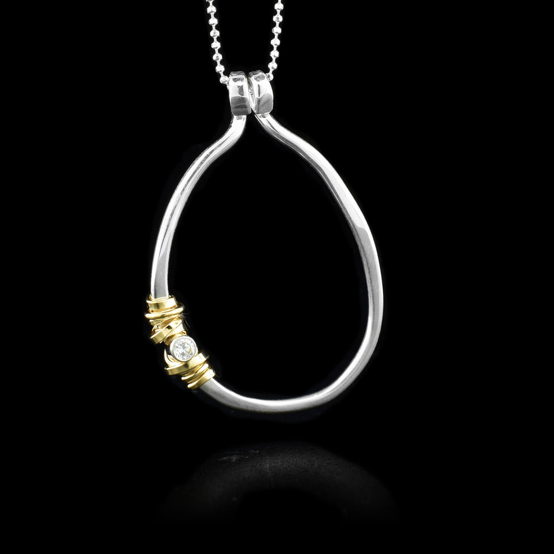 This unique pendant necklace has a sterling silver, circle shaped pendant with gold fill embellishments wrapped around it. By the gold fill is a cubic zirconia gemstone.