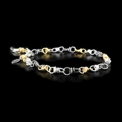 This sterling silver and gold fill chain bracelet has intricate links that transition from silver, gold, and silver ones with a coil design.