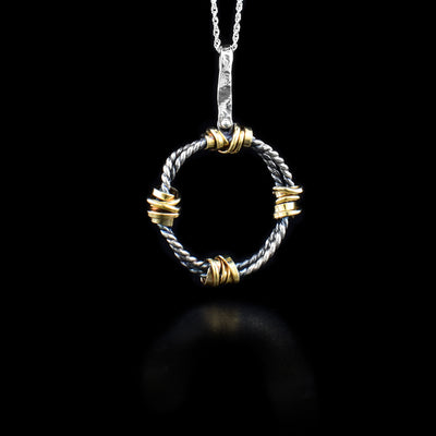 This sterling silver circle pendant necklace has a long jump ring attached to a coil circle. There are four gold-fill wraps on the pendant.