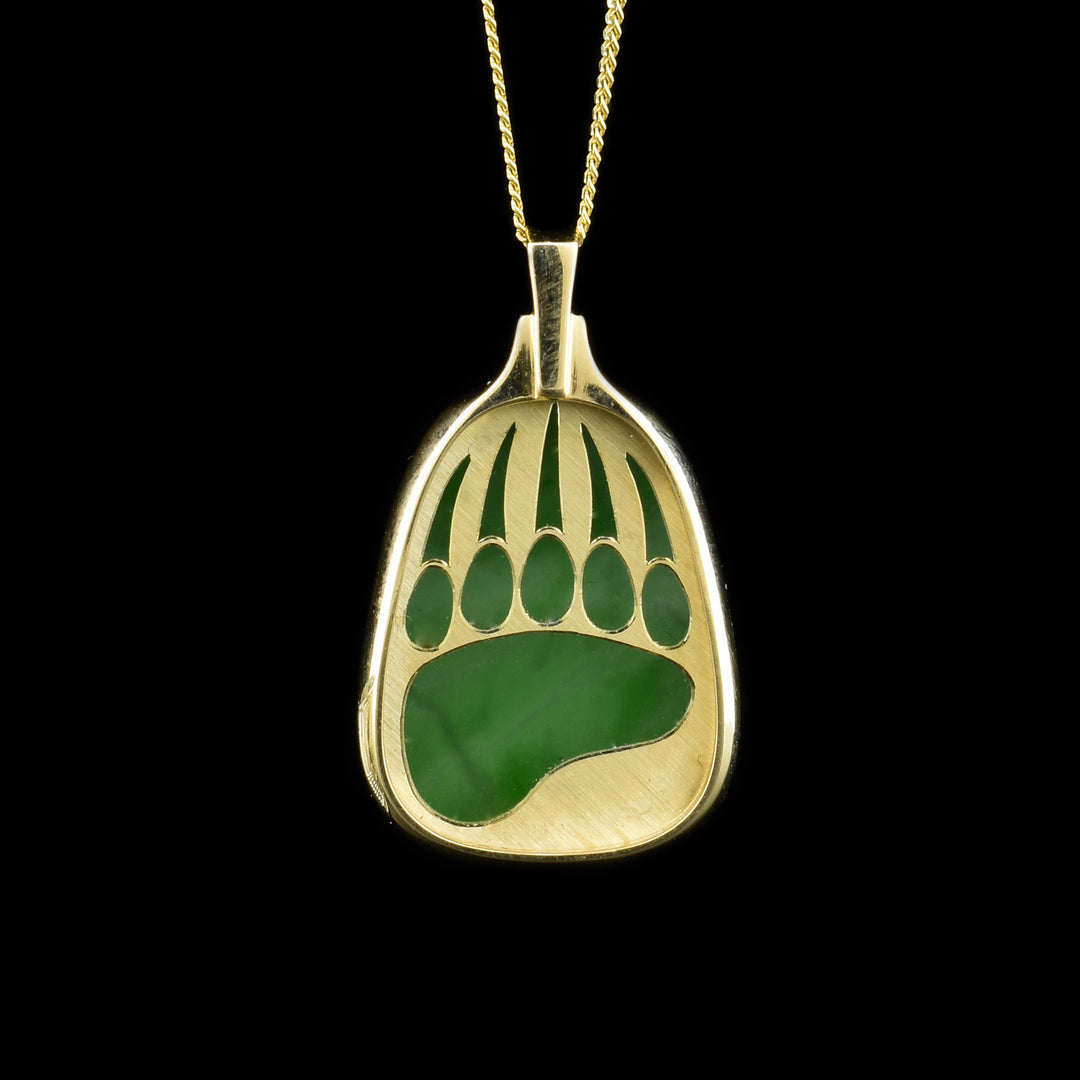 A jade bear paw pendant that has a layer of gold on top with a jade stone underneath. The layer of gold has a bear print cut out, so the jade is visible underneath.