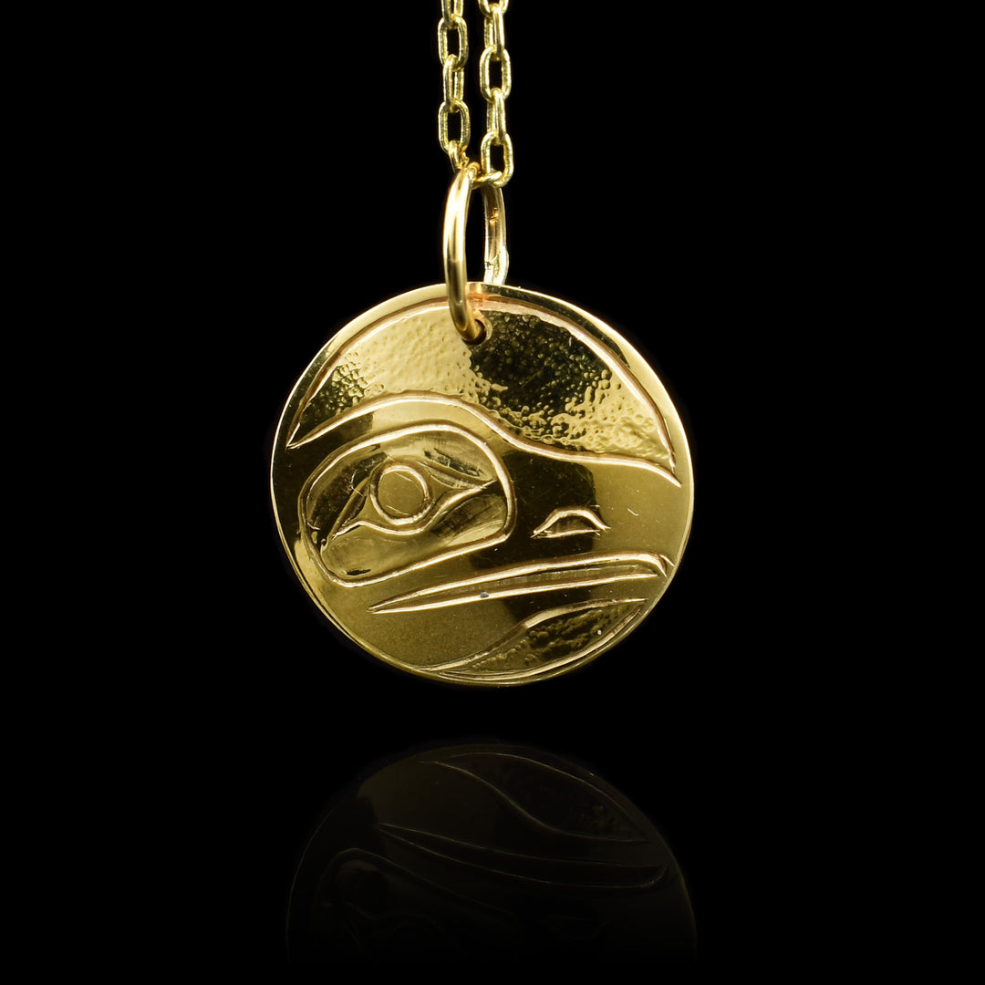 This 18K gold pendant is circle shaped and has a depiction of the Raven carved into the surface of it.