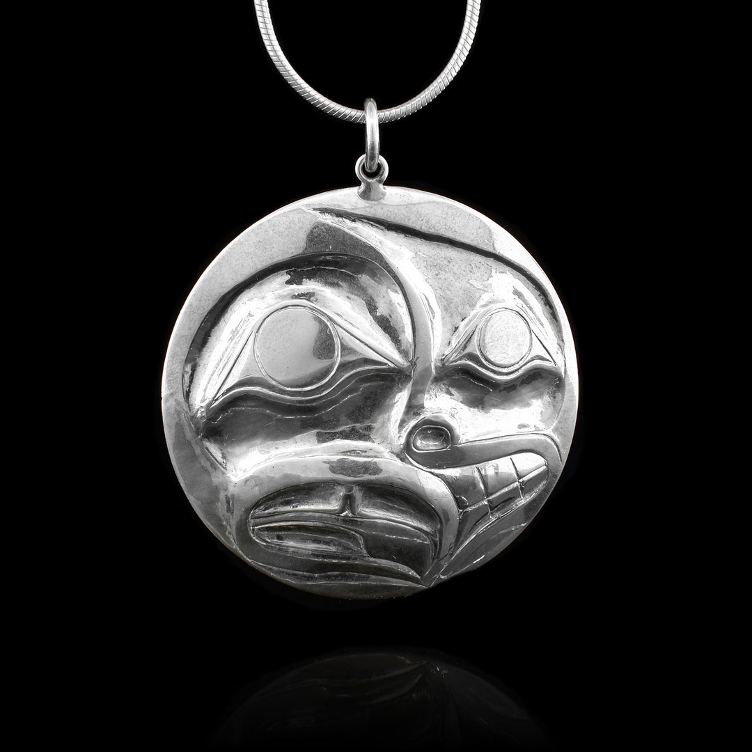 This sterling silver pendant is circlular and has been shaped using a repousse method. Half the pendant depicts a person and the other half depicts the Raven legend.