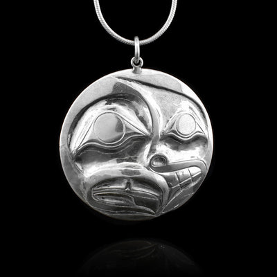 This sterling silver pendant is circlular and has been shaped using a repousse method. Half the pendant depicts a person and the other half depicts the Raven legend.