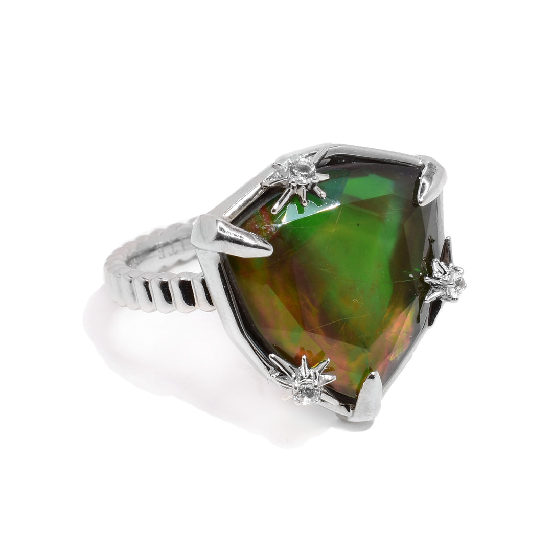 This ammolite ring is made from sterling silver, has a thin band, and has a large, shield shaped ammolite gem in the center. There are silver embellishments with topaz gems around the ammolite gem.