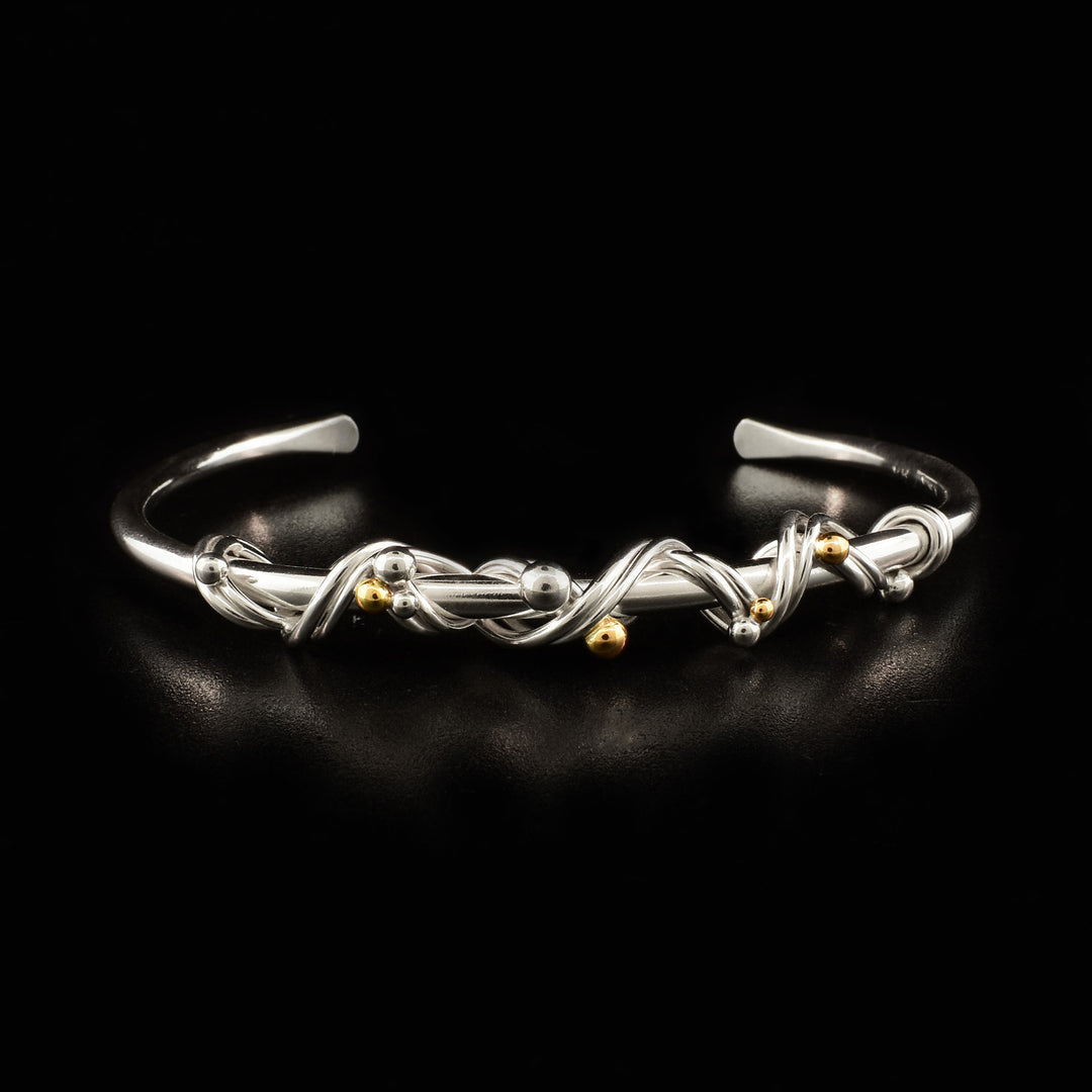 Thin, sterling silver bangle with sterling silver wire wrapped around front. Small 14K gold and sterling silver balls interwoven in wire.