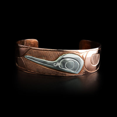 Front of bracelet depicts side-view of sterling silver hummingbird head pointing right. Rest of piece is copper. Designs done in ovoids and lines depict hummingbird’s body and a flower. Backdrop is cross-hatching.