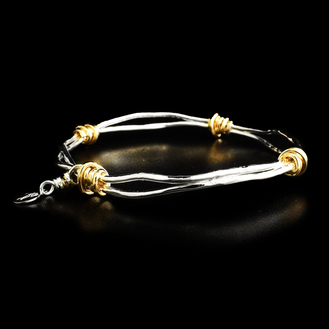 This sterling silver bangle bracelet is made from thick, sliver wires that wrap around each other and has gold fill embellishments wrapped around the bracelet.