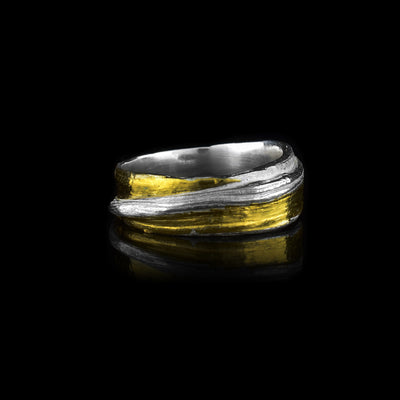 This dainty silver ring is made from sterling silver and has flowing designs on the surface of it. The piece is made by casting metal into wax so it mimics the appearance of its wax mold. There are keum boo gold highlights on the band around one of the wavy strips of sterling silver.