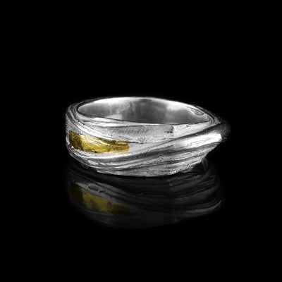 This wavy ring band is made from sterling silver and has flowing designs on the surface of it. The piece is made by casting metal into wax so it mimics the appearance of its wax mold. There are keum boo gold highlights on the band around one of the strips of sterling silver.