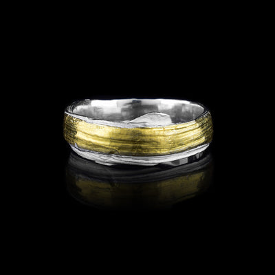 This thin silver band ring is made from sterling silver and has flowing designs on the surface of it. The piece is made by casting metal into wax so it mimics the appearance of its wax mold. There are keum boo gold highlights on the band around the center of the band.