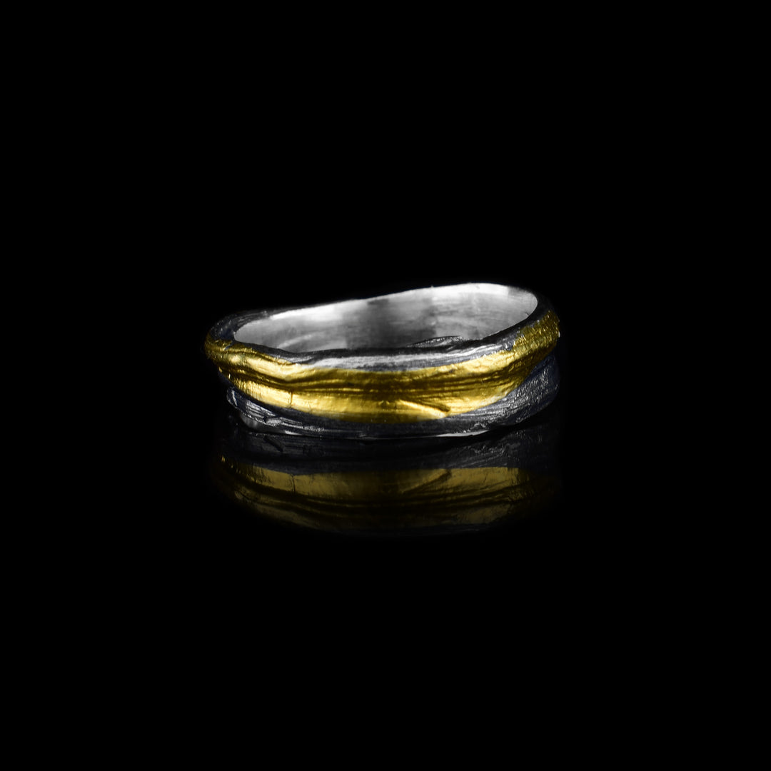 This dainty silver ring is made from sterling silver and has flowing designs on the surface of it. The piece is made by casting metal into wax so it mimics the appearance of its wax mold. There are keum boo gold highlights on the band across the wavy strips of sterling silver.