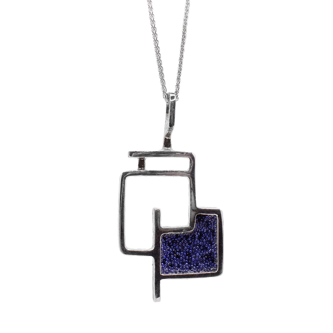 This silver necklace is made of oxidized silver and has abstract rectangle designs. One of the rectangles is filled with a blue design.