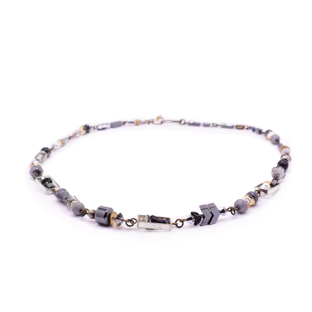 This piece masterfully blends industrial geometric frames with an organic array of faceted crystals, matte hematite, and lava-style beads. Designed with a sophisticated smoky palette, its 50cm length.