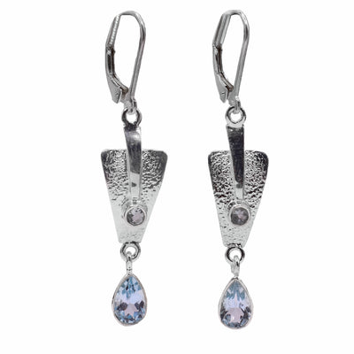   These blue topaz drop earrings have upside down, triangle hangs dangling from the hooks. There are teardrop shaped gems dangling from the triangle pieces which also have a textured surface. 