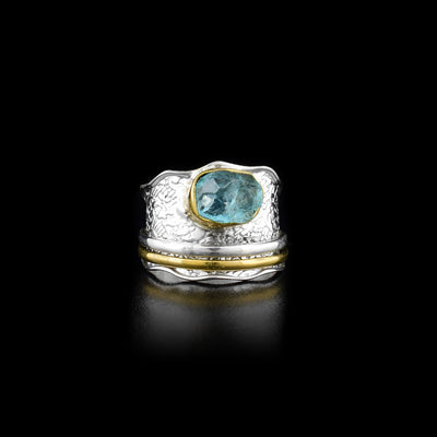 This spinner ring is made from sterling silver, brass and apatite gemstone. There is a wavy, tapered and silver band with designs imprinted on it and the large gem placed on top of the band. There is a silver hoop and brass hoop on the band that can be spun around the piece.