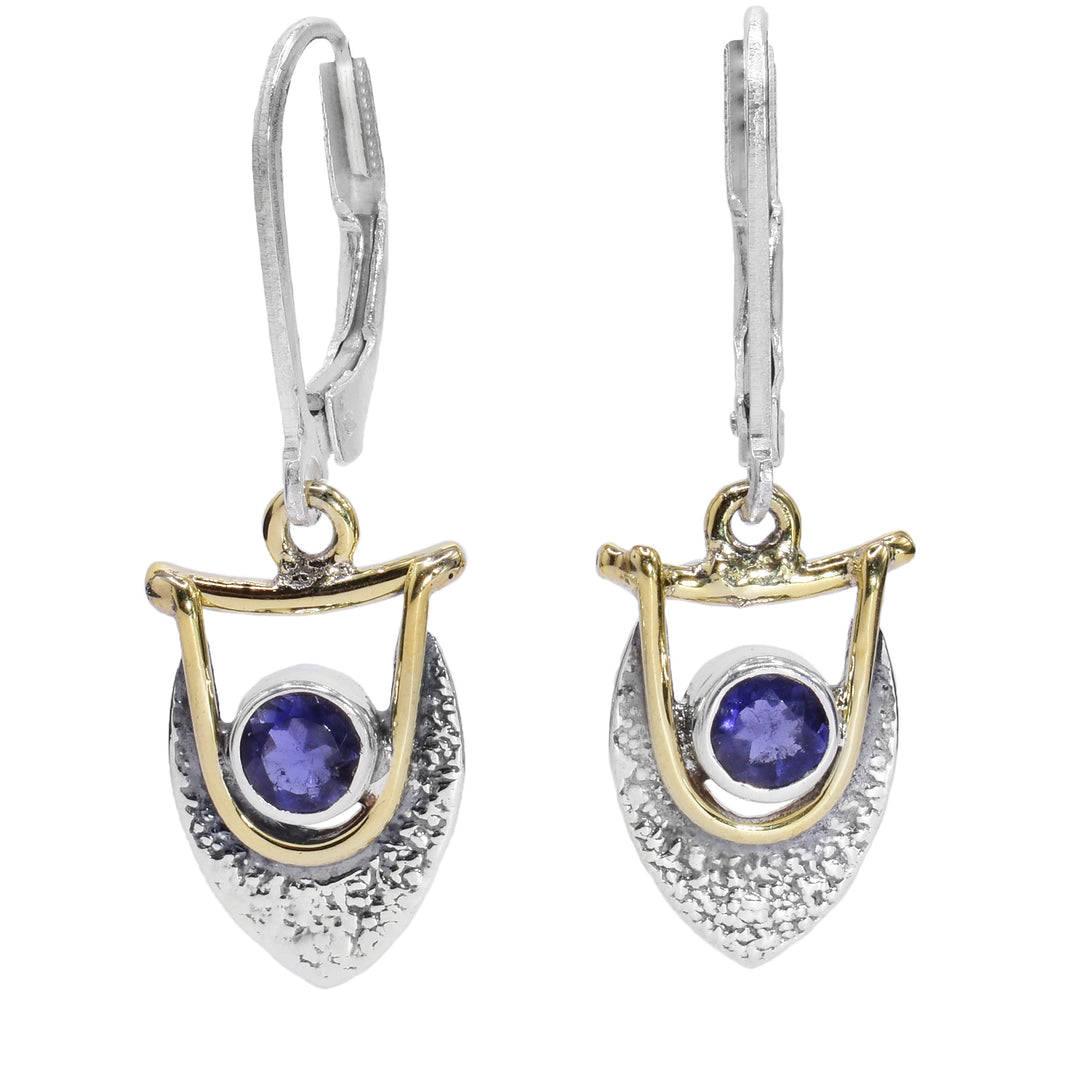 These iolite earrings are made from sterling silver, brass and purple iolite gemstones. The hangs have a teardrop shaped, textured silver piece with purple gems held at the top of them. There is brass wire wrapped around the gems and connect to the hooks.