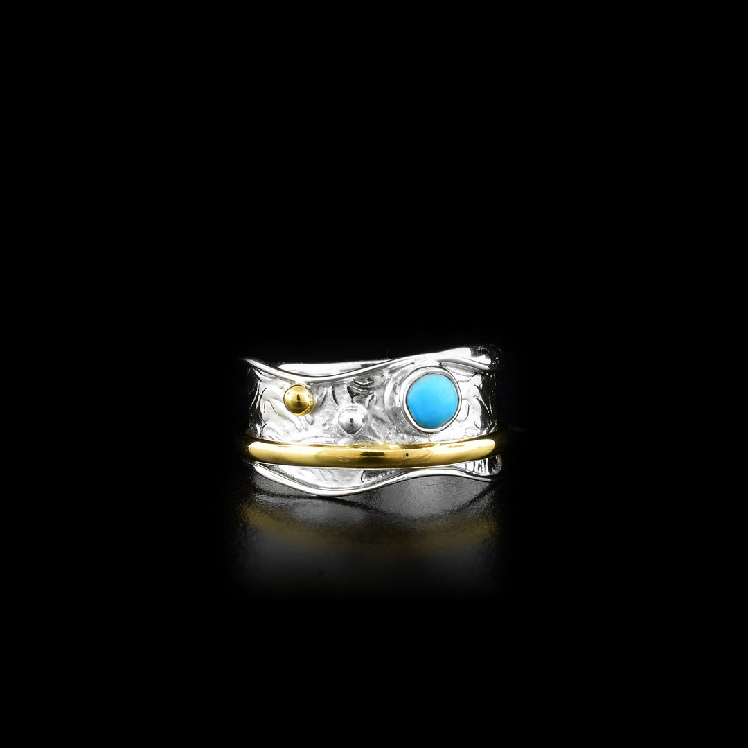 This spinner ring is made from sterling silver, brass and turquoise gemstones. There is a wavy silver band with a turquoise gem and brass beads on the surface of it. There is a brass hoop on the band that can be spun around the piece.