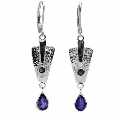   These purple iolite gemstone dangle earrings have upside down, triangle hangs dangling from the hooks. There are teardrop shaped gems dangling from the triangle pieces which also have a textured surface. 