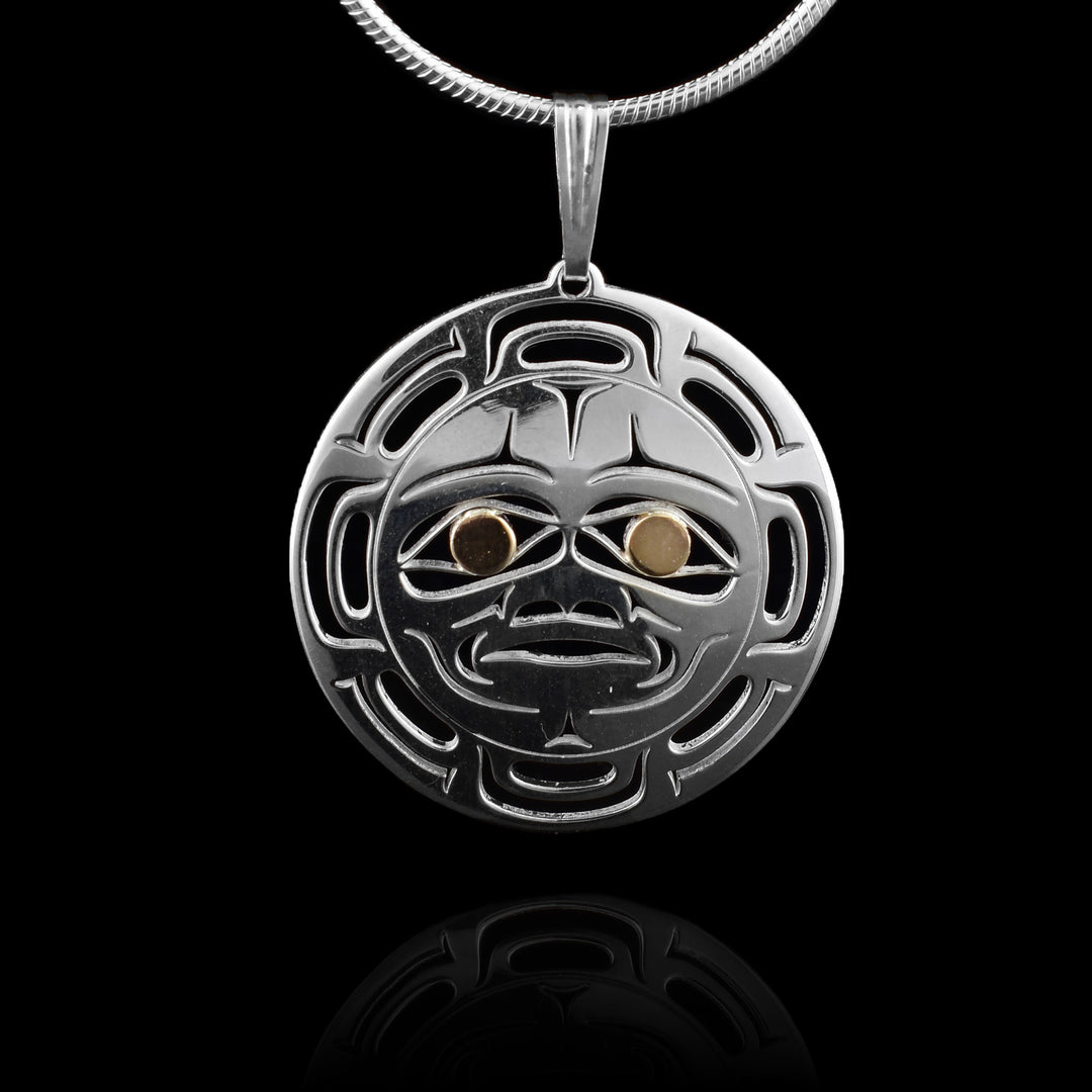 This Moon pendant necklace has a circle shape and is made from sterling silver. There are cutout designs depicting the face of the moon in the center with its eyes, eyebrows, nose and mouth detailed. Surrounding the face, there are "moon ray" designs. The eyes of the legend are made from 14k gold.