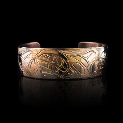 This copper cuff bracelet has a wide band with a depiction of three, Orca legends carved into the surface of it. The Orcas are depicted in side view with ocean wave designs made around the Orca pod.